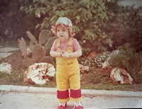 a child in overalls standing in front of a cactus